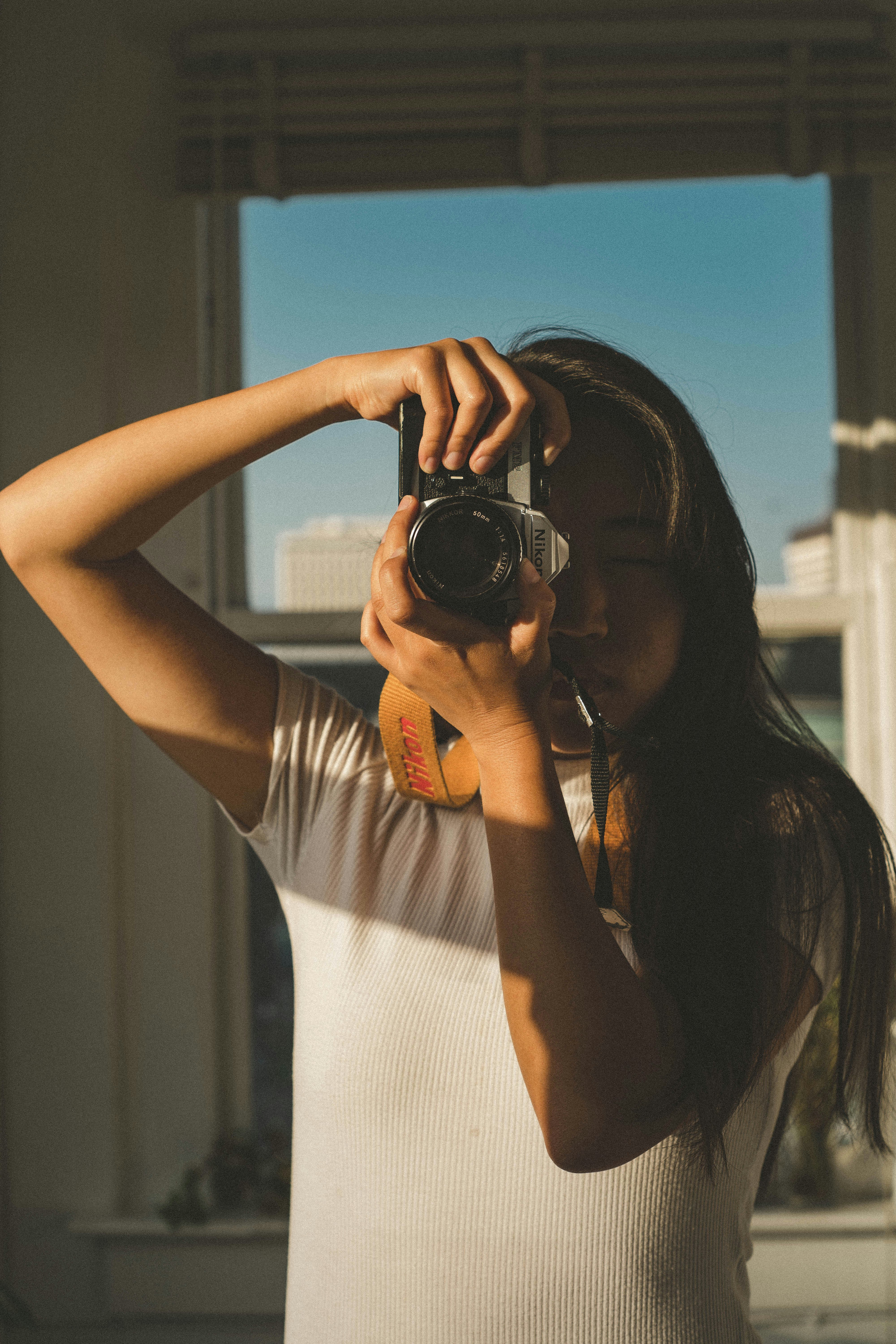 woman in white tank top holding black dslr camera